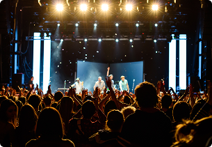Artiesten treden op op een helder verlicht podium van Moen feest voor een enthousiast publiek, tijdens een feestelijk event met X²O badkamers als partner.